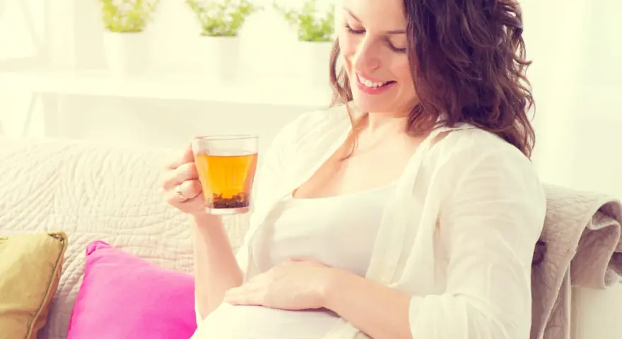 Femme enceinte souriante tenant une tasse d'infusion de thym, posant sa main sur son ventre.