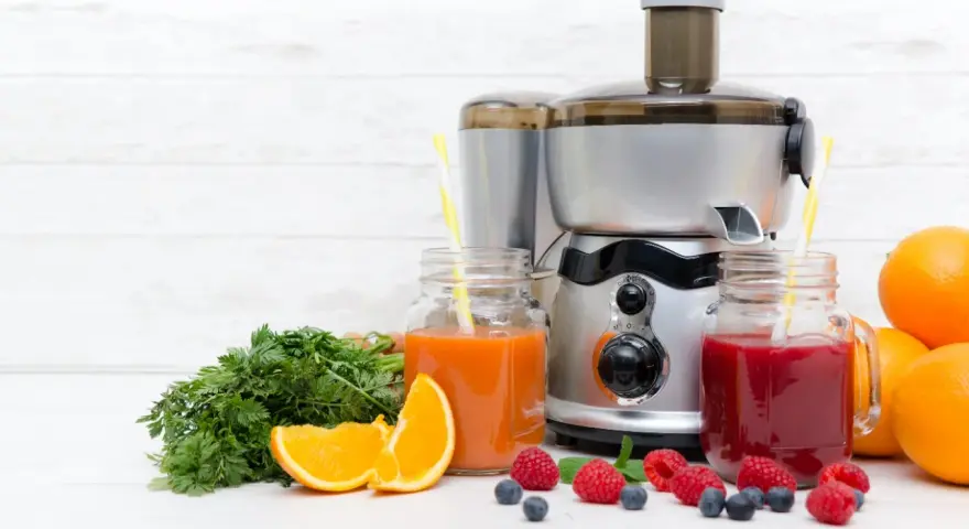 Une centrifugeuse ou extracteur prépare des jus frais avec des fruits et légumes. Ici, des jus d'orange, de carotte et de baies, avec des oranges, des carottes et des baies.