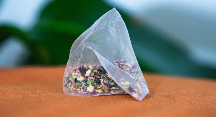 Un sachet de tisane pour anémie, rempli d'herbes et de pétales de fleurs colorés, repose sur un tissu orange.