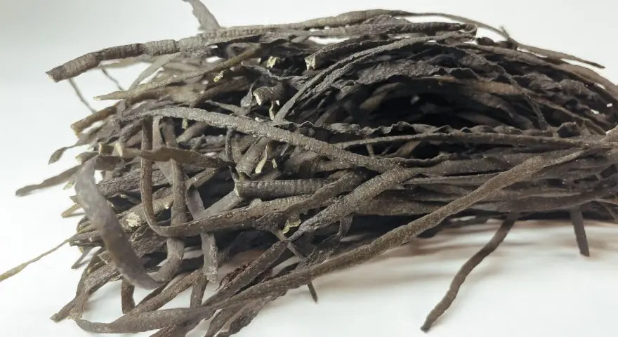 Un tas de spaghetti de mer séchés, ressemblant à des fils sombres et ondulés, prêts à être réhydratés pour un plat savoureux.