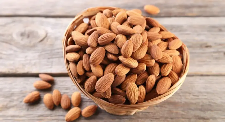 Un panier rempli d'amandes sur fond de bois. Savoir pourquoi faire tremper les amandes améliore leur digestibilité et leur saveur.