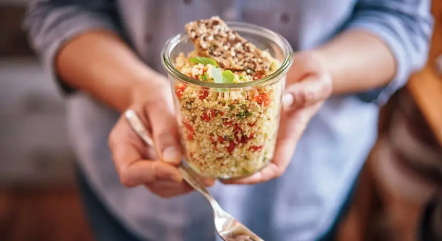 Un bocal rempli de quinoa coloré, parfait pour un régime sain. Une fourchette est prête à déguster ce plat savoureux.