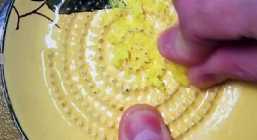 Main d'une personne râpe du gingembre sur une râpe jaune décorée.
