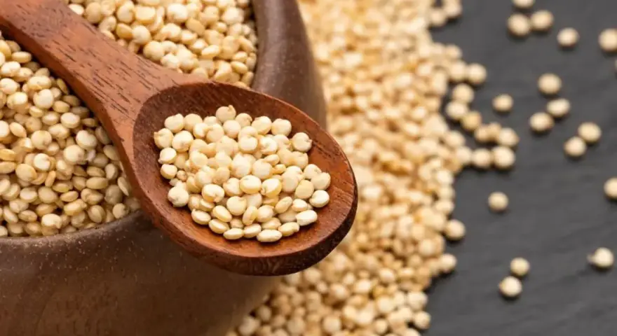 Une cuillère en bois remplie de quinoa cru, posée sur un bol débordant de ces graines nutritives.