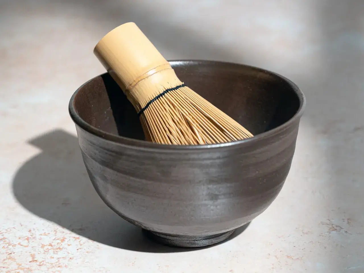Un fouet en bambou, ou chasen, repose dans un bol en céramique sombre, prêt à préparer un matcha latte.