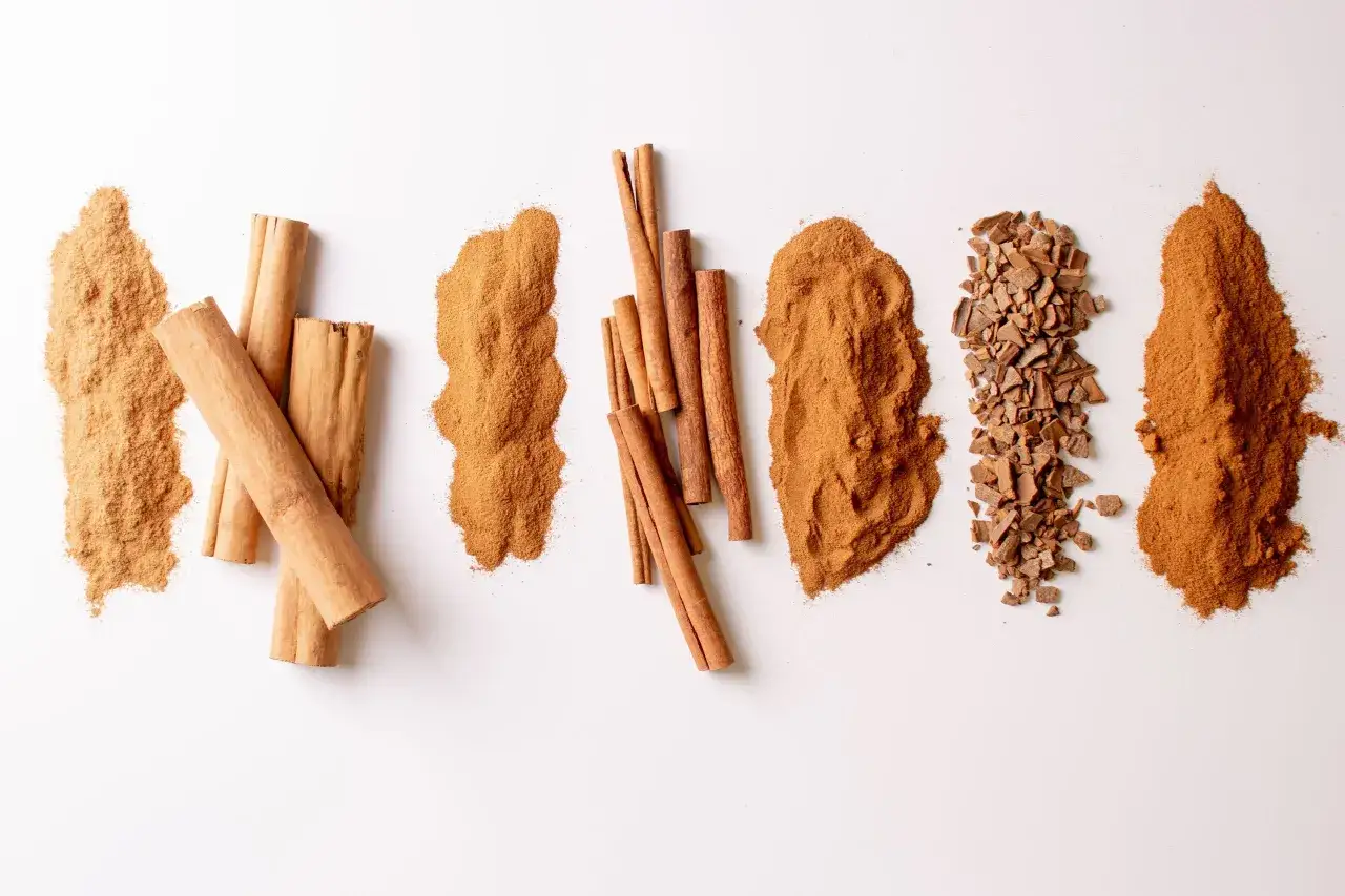 Piles de cannelle en poudre, b&acirc;tons et &eacute;clats sur fond blanc. Un d&eacute;lice pour les sens.