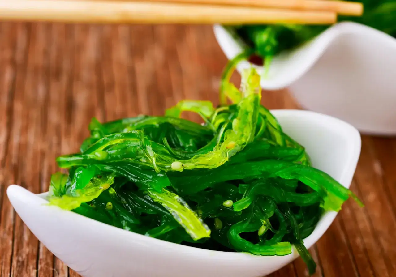 Salade d'algue de mer verte et brillante, servie dans un bol blanc, pr&ecirc;te &agrave; &ecirc;tre d&eacute;gust&eacute;e avec des baguettes.