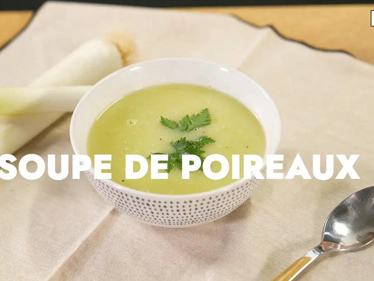 Un bol de soupe de poireaux onctueuse, garnie de persil frais, avec des germes de poireaux en arri&egrave;re-plan.