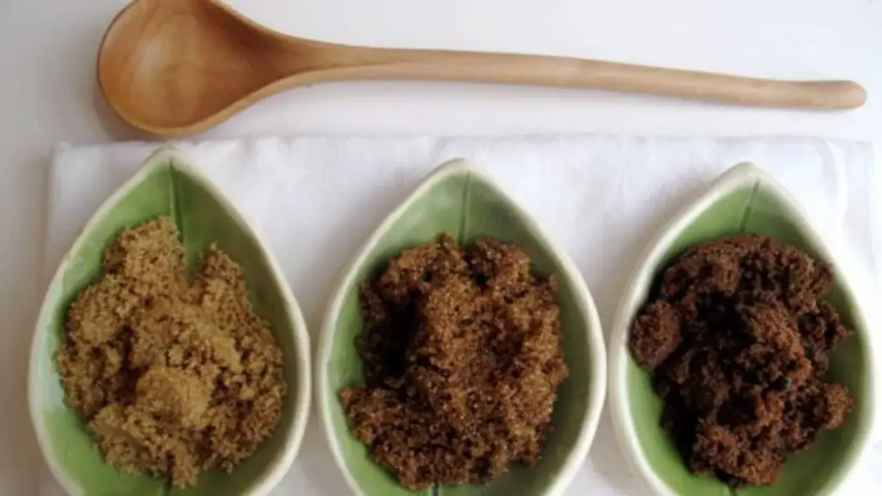 Trois coupelles en forme de feuille verte contiennent du sucre muscovado de diff&eacute;rentes teintes. Une cuill&egrave;re en bois repose au-dessus. D&eacute;couvrez les sucre muscovado bienfaits !