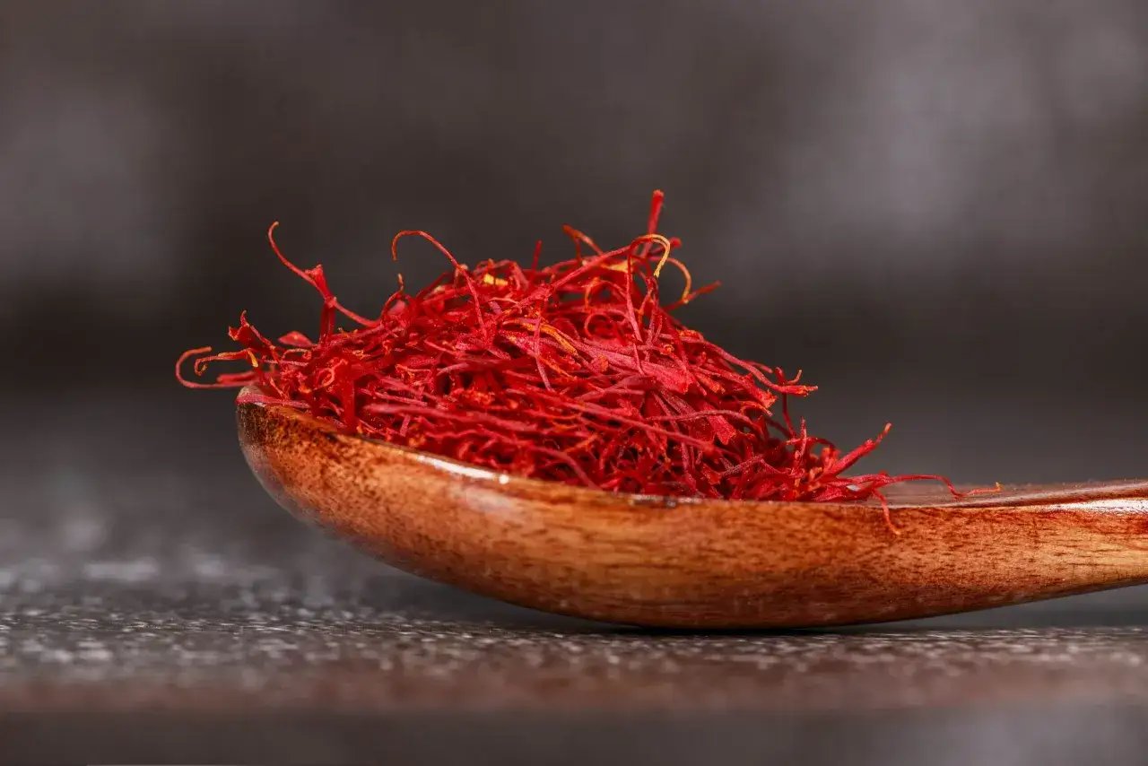 Une cuill&egrave;re en bois remplie de filaments de safran rouge vif, &eacute;voquant ses nombreux safran bienfaits pour la sant&eacute; et la cuisine.