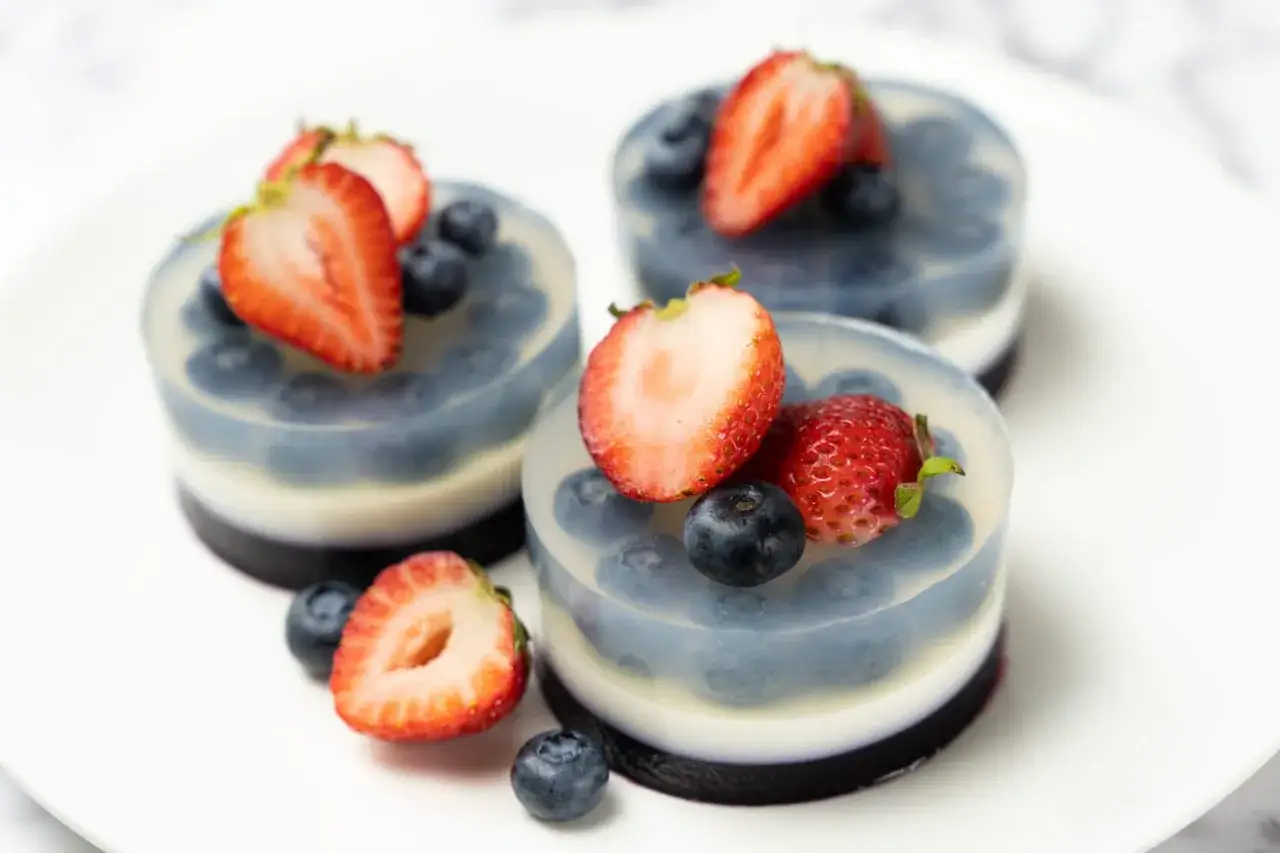 Trois délicieux desserts aux fruits, à base d'agar agar, ornés de fraises et de myrtilles fraîches sur une assiette blanche.