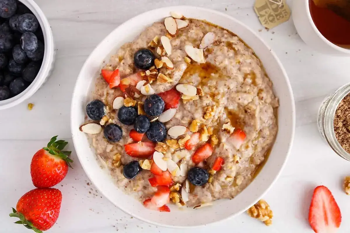 Bol de porridge aux fruits rouges, myrtilles, amandes effilées et noix, arrosé de miel. Une touche de graine de lin pour un petit-déjeuner sain.