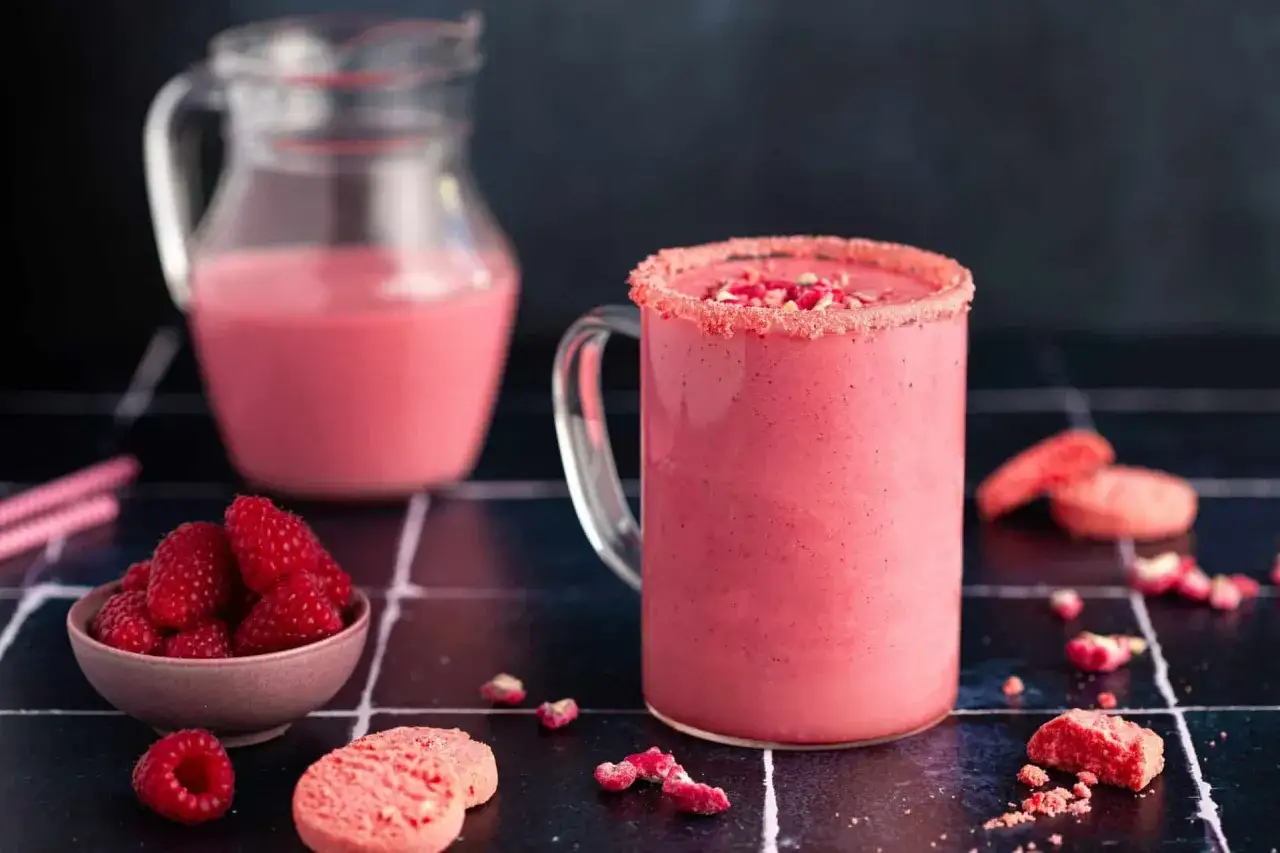 Un délicieux milkshake aux framboises, parfait pour une recette facile et gourmande. Des framboises fraîches et des biscuits complètent ce visuel appétissant.