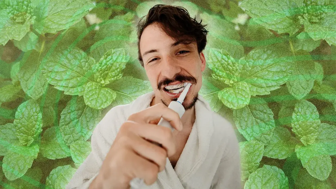 Un homme se brosse les dents avec une brosse électrique, entouré de feuilles de menthe, rappelant les menthe bienfaits pour la fraîcheur.
