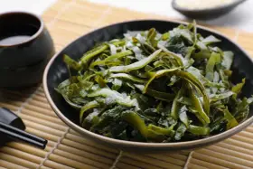 Un bol de salade d'algues kombu, aux multiples algue kombu bienfaits, servi avec une sauce et des baguettes sur un tapis de bambou.