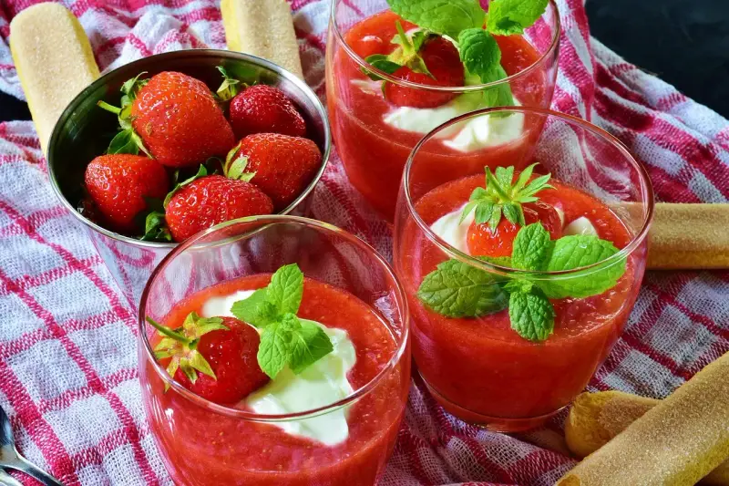 Trois coupes de coulis de fraise, garnies de crème et de menthe, avec des fraises fraîches dans un bol.