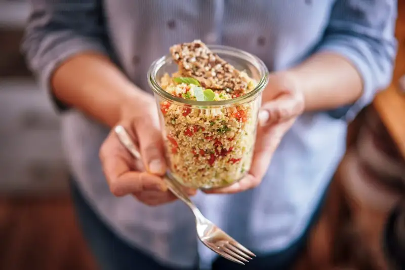 Un bocal rempli de quinoa coloré, parfait pour un régime sain. Une fourchette est prête à déguster ce plat savoureux.